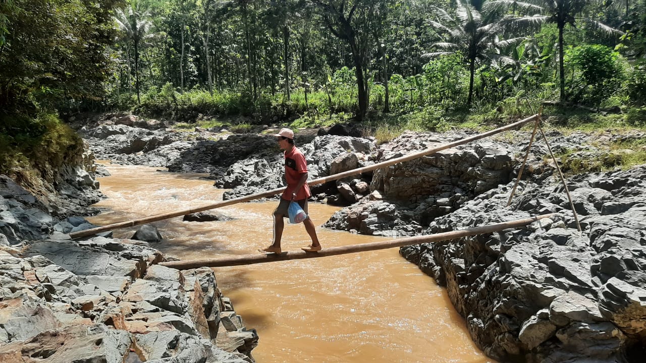 Warga saat melintasi sungai dengan sebatang bambu.